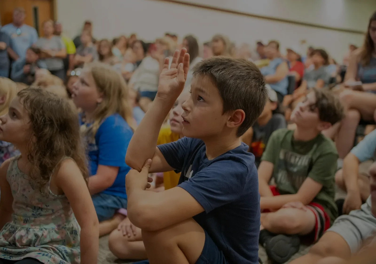 Children seated on the floor raising their hands during a story hour reading